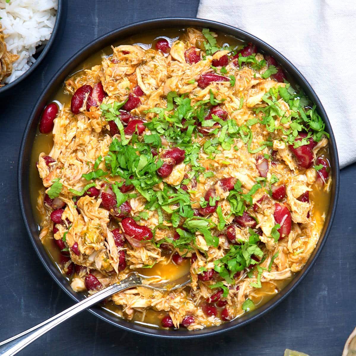 Mexican shredded chicken with salsa verde in dark bowl with spoon over rice.