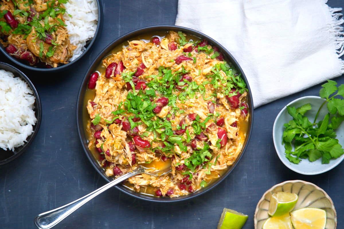 Mexican shredded chicken with salsa verde in dark bowl with limes on the side.