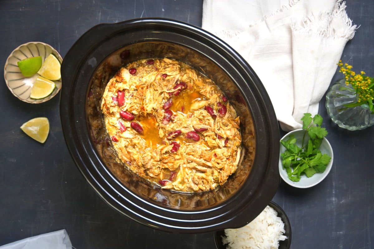 Cooked Mexican shredded chicken with salsa verde in slow cooker.