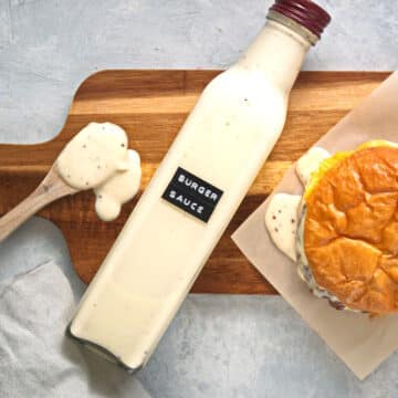 Smoky maple burger sauce in glass bottle with a burger and spoon full of sauce on the side.