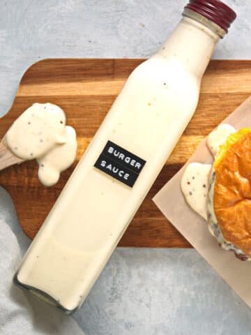 Smoky maple burger sauce in glass bottle with a burger and spoon full of sauce on the side.