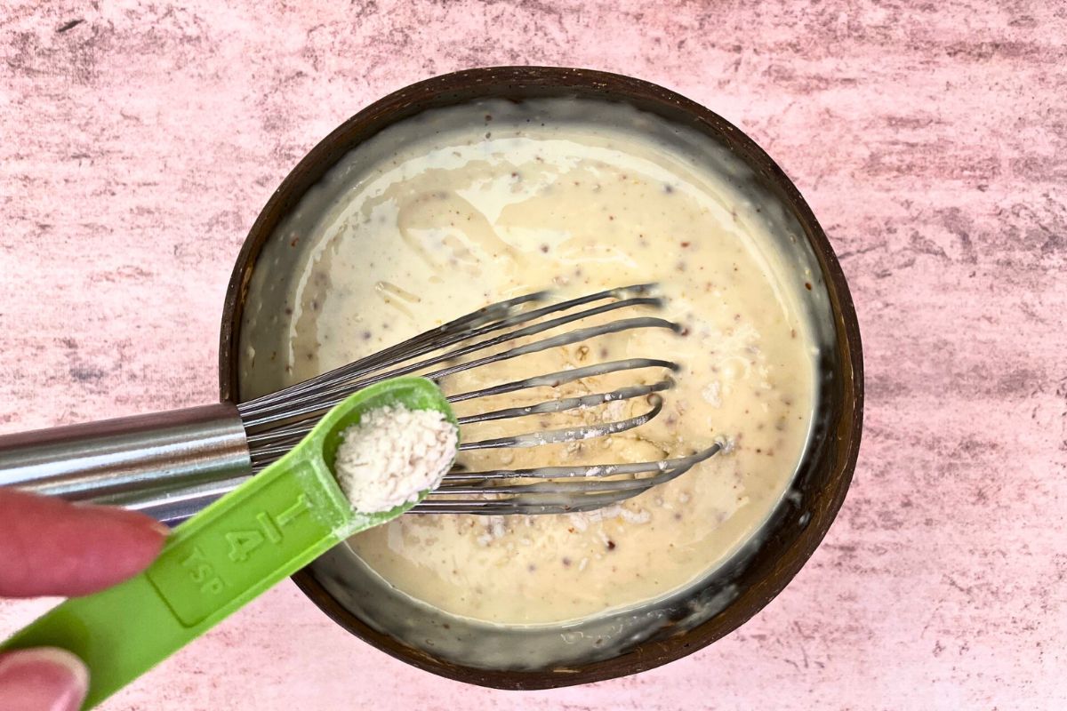 Guar gum getting sprinkled into bowl of smoky maple burger sauce with whisk.