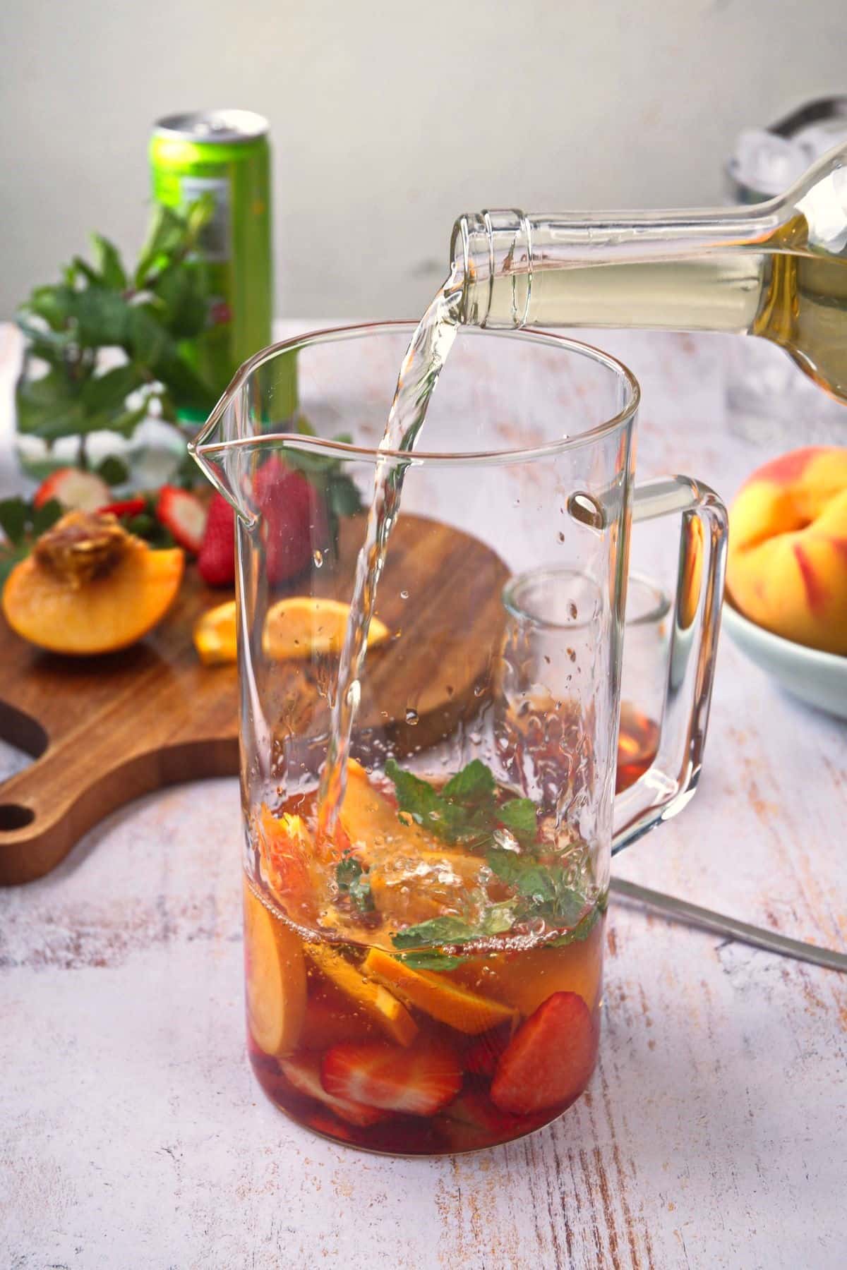 White wine pouring into pitcher filled with fresh fruit.