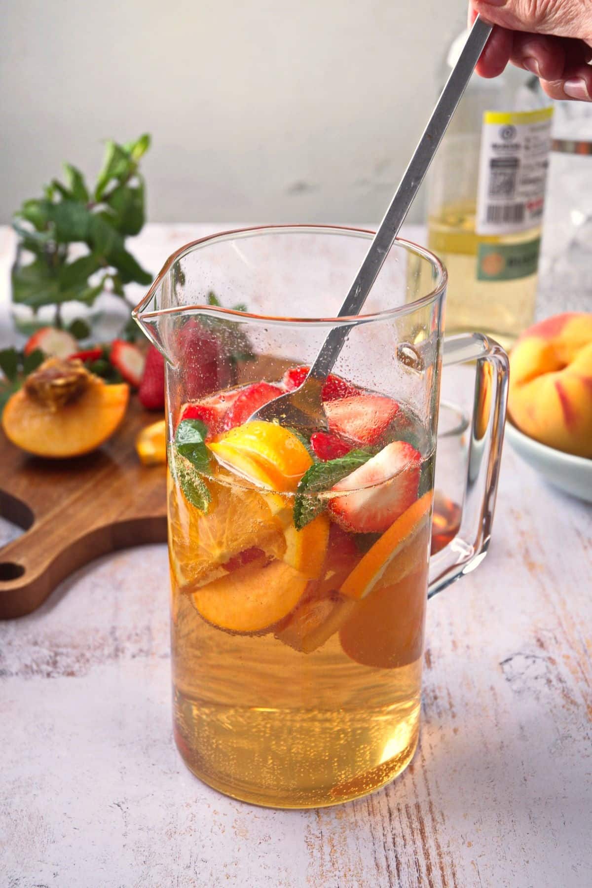 Spring sangria getting mixed with spoon in glass pitcher.