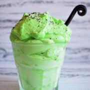 Green peppermint whipped cream in glass with curled black spoon.