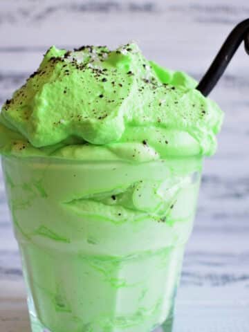 Green peppermint whipped cream in glass with curled black spoon.