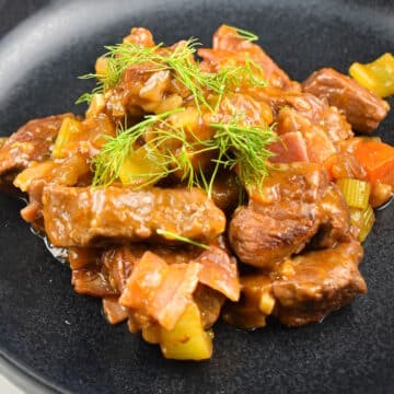 Beef black beer stew on black plate with fresh dill.