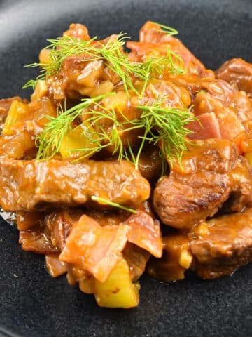 Beef black beer stew on black plate with fresh dill.