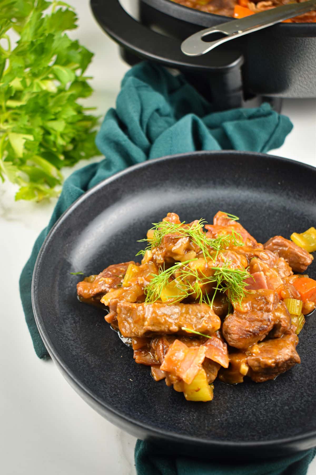 Beef black beer stew on black plate with skillet in background.