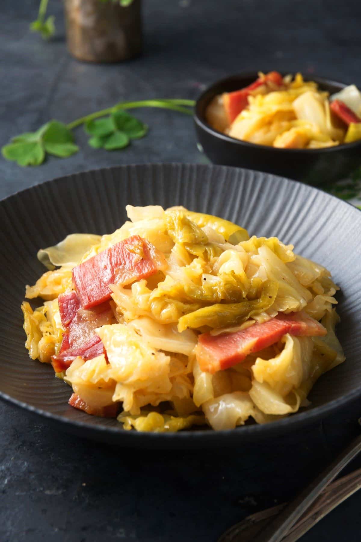 Cooked cabbage and bacon in black bowl.