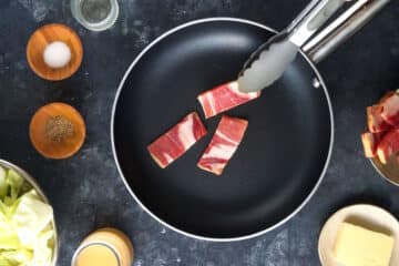 Raw bacon strips in pan with tongs.