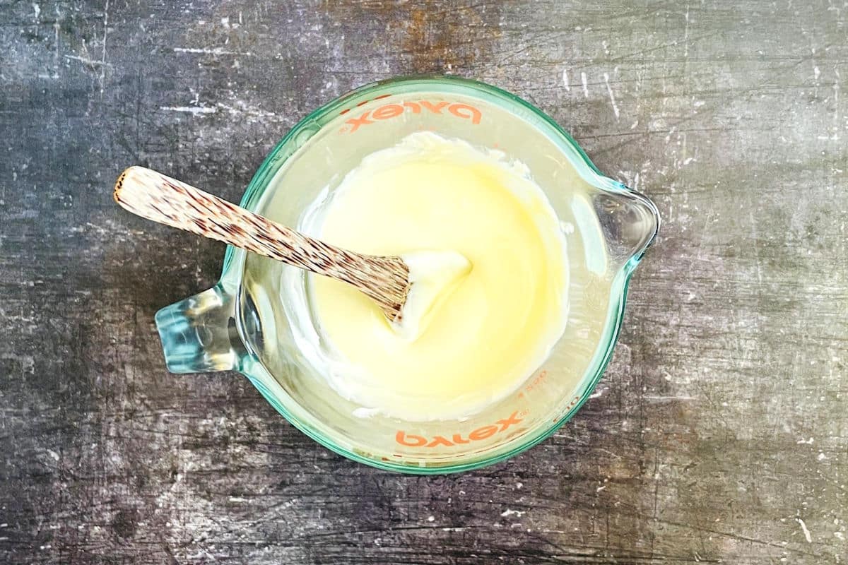 White chocolate melted in measuring glass with small wooden spoon.