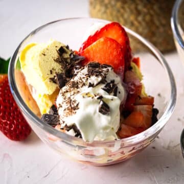 Strawberry ice cream sundae with chocolate shavings in curved bowl.