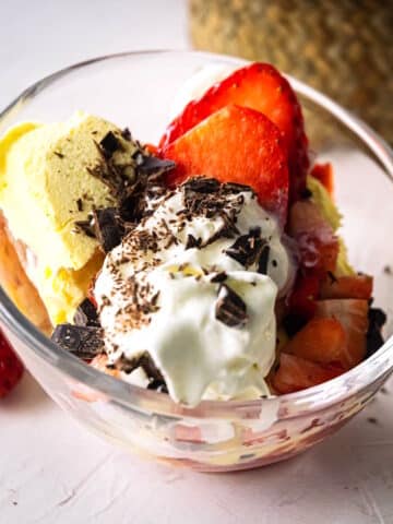 Strawberry ice cream sundae with chocolate shavings in curved bowl.