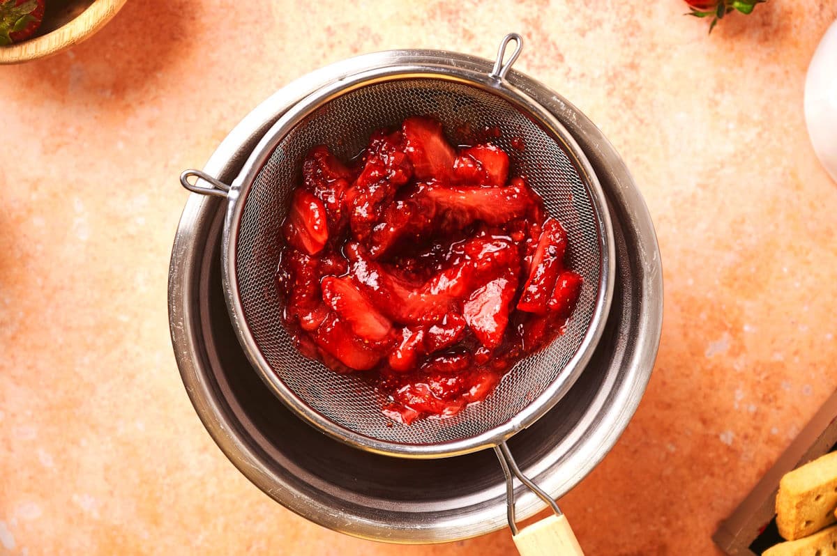 Strawberry sauce straining through fine mesh strainer.