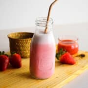 Homemade strawberry milk with straw in jar on cutting board.