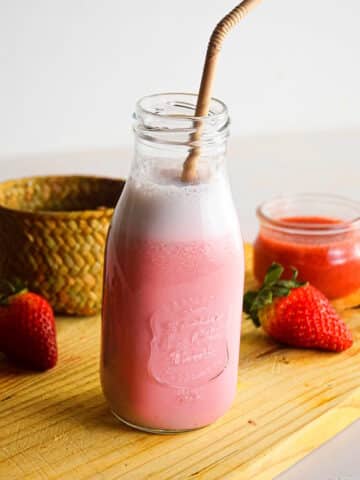 Homemade strawberry milk with straw in jar on cutting board.