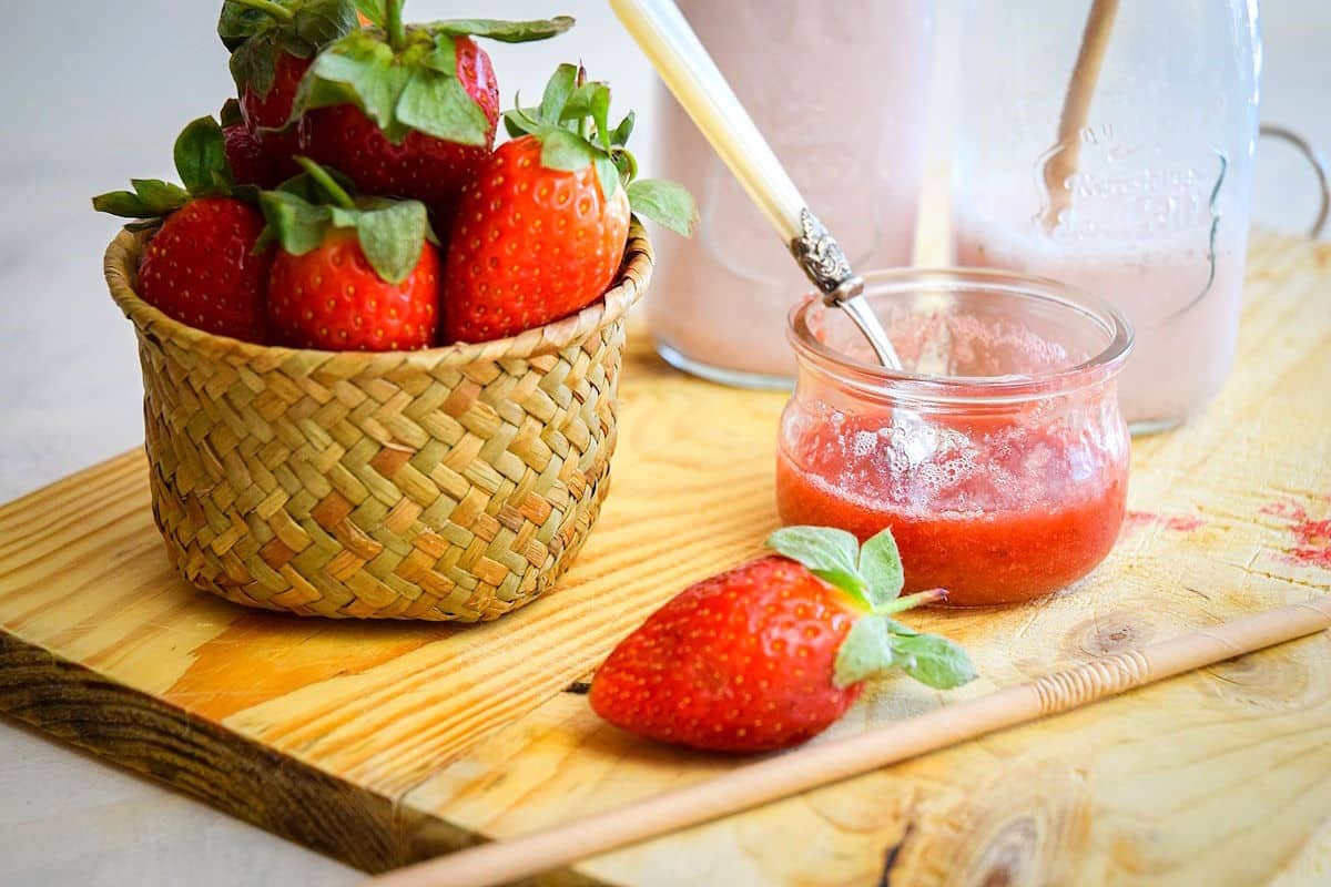 Fresh strawberries, milk and strawberry syrup on cutting board.
