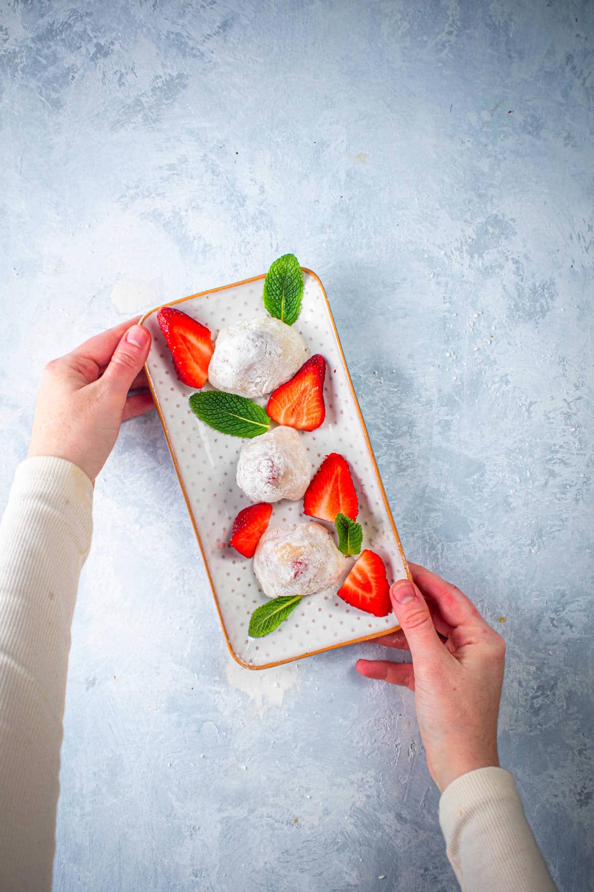 Serving plate filled with strawberry mochi, mint leaves and fresh sliced strawberries.