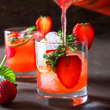 Strawberry mojito mocktail pouring out of pitcher into glass with ice cubes.