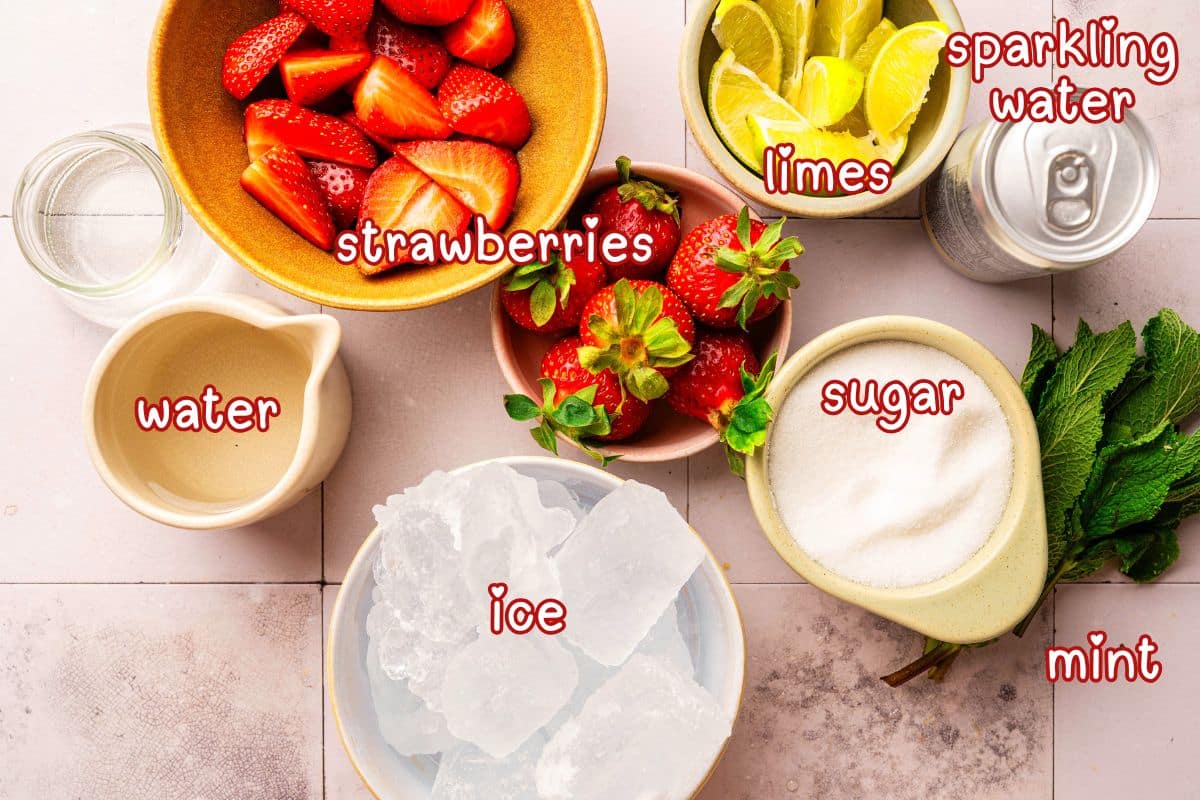 Strawberry mojito mocktail ingredients prepped on light tile background.