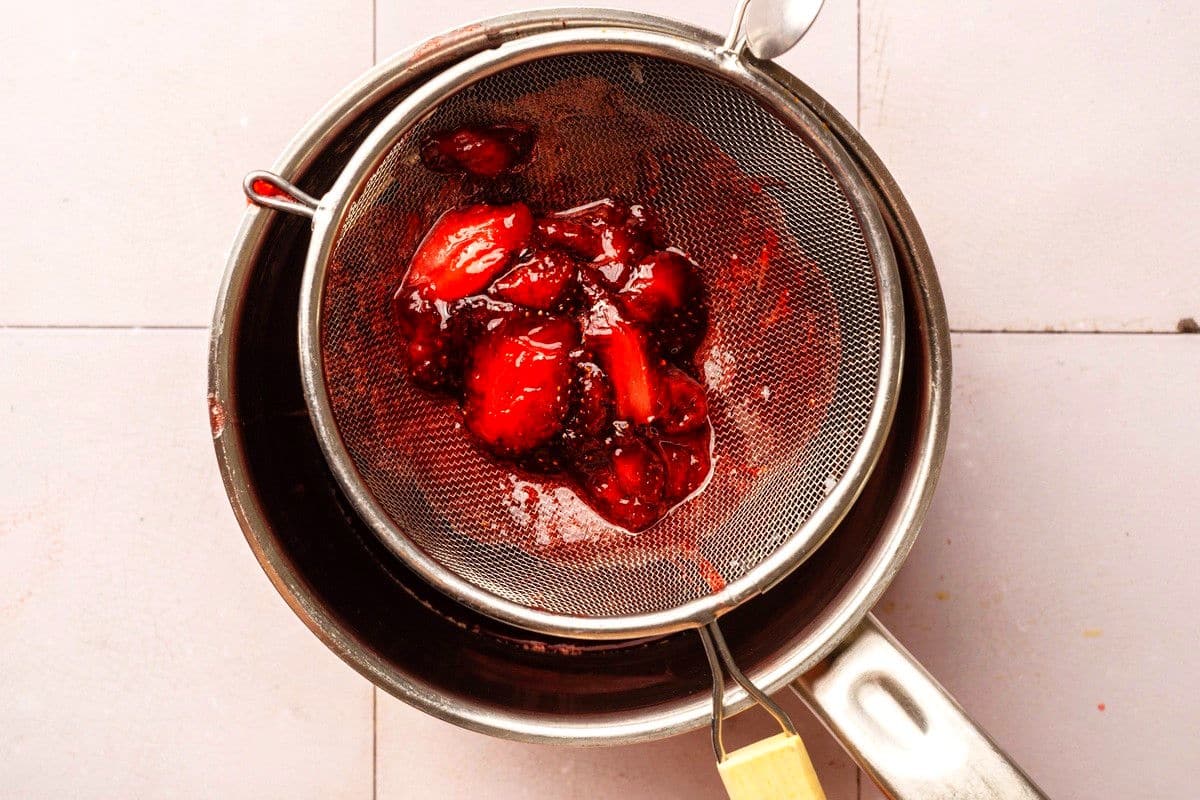 Strawberry syrup straining into pot through fine mesh strainer.