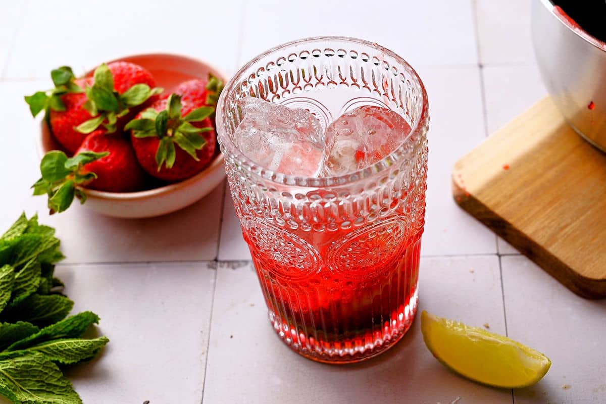 Glass with strawberry mojito mocktail ingredients and ice.