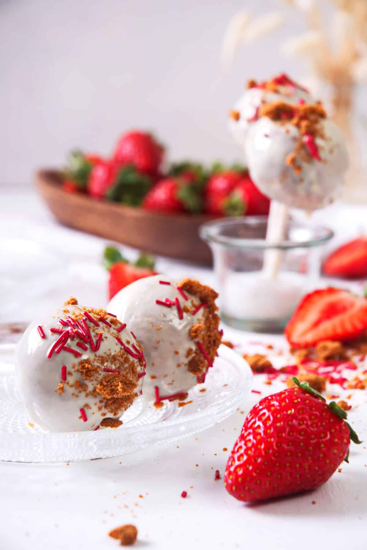 Strawberry shortcake pops with fresh strawberries on clear glass plate.