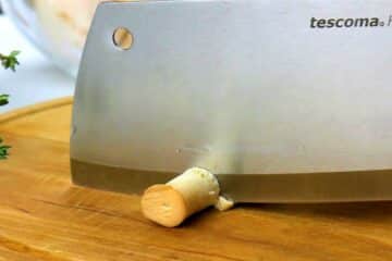 Butcher knife slicing a button mushroom.