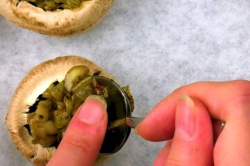 Uncooked button mushrooms getting stuffed with filling.