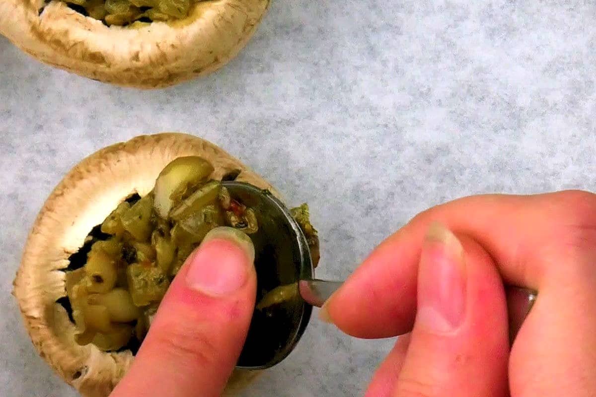 Uncooked button mushrooms getting stuffed with filling.