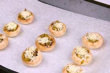 Stuffed uncooked button mushrooms on parchment lined baking sheet.