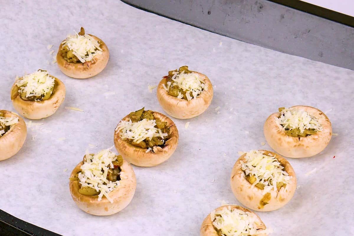 Stuffed uncooked button mushrooms on parchment lined baking sheet.