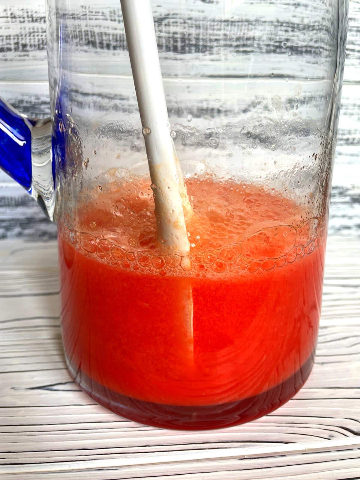 Summer mango pomegranate soda in glass pitcher with stirring spoon.
