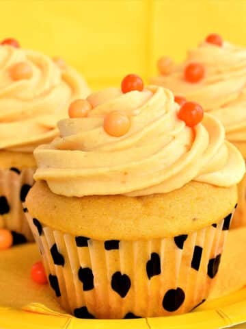 Moist, frosted pumpkin cupcakes on yellow plate.