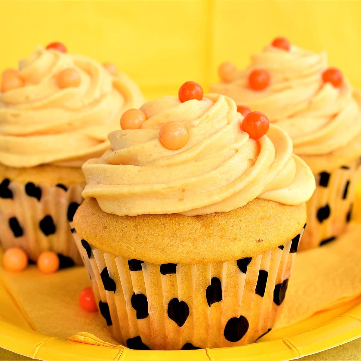 Moist, frosted pumpkin cupcakes on yellow plate.