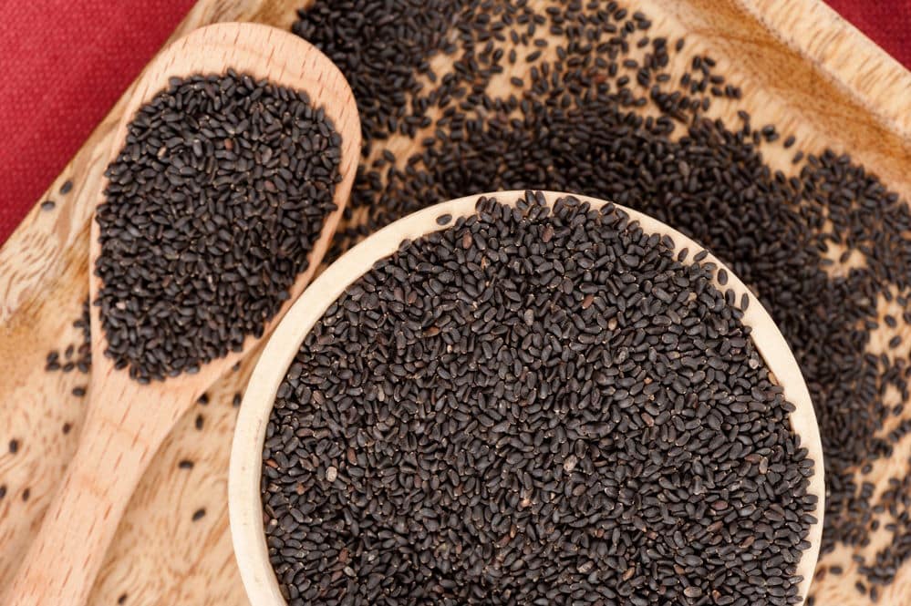 Closeup of sweet basil seeds in a bowl and wooden spoon.