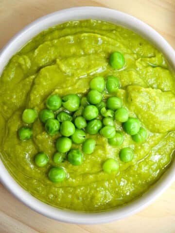 Pea purée in white dish with whole peas and olive oil on top.