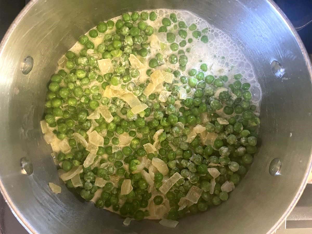 Peas, onions and cream mixture cooking in pot.