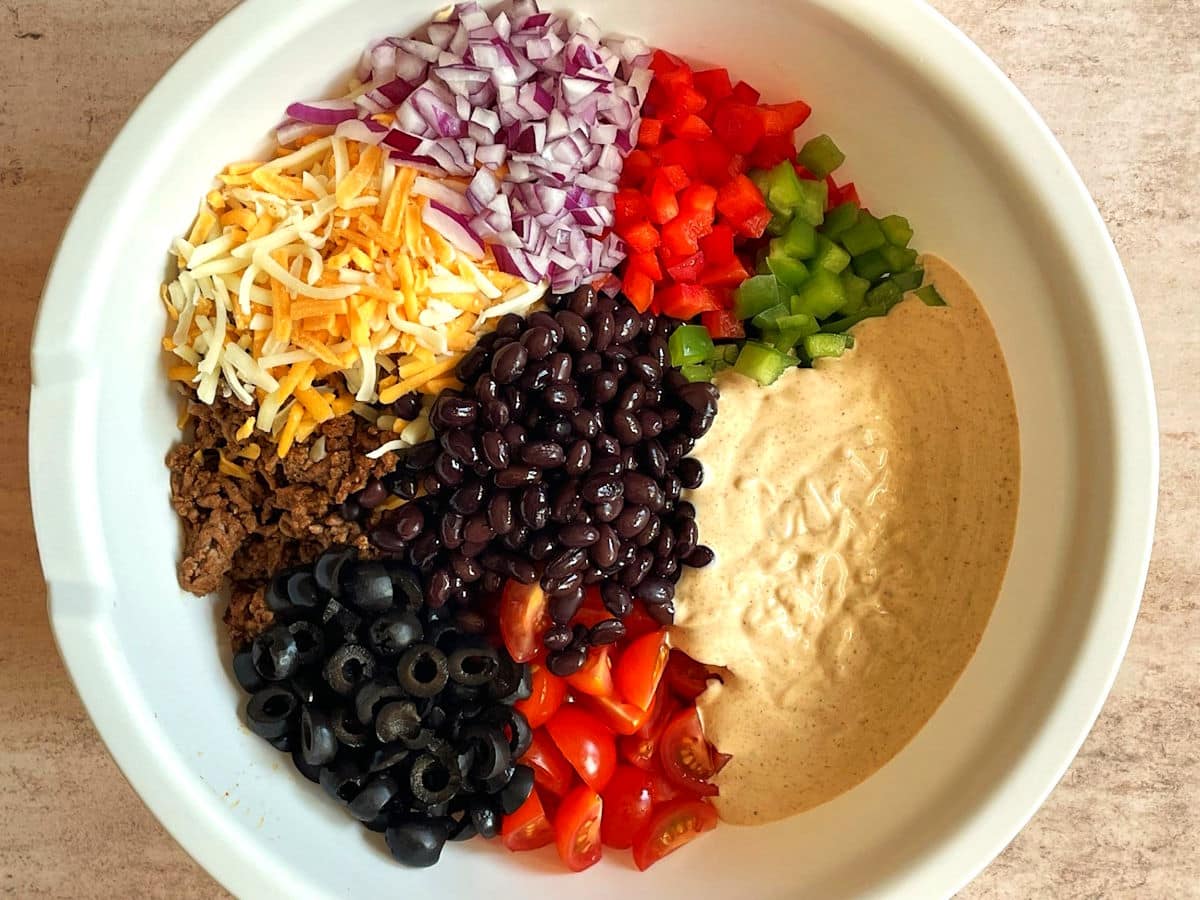 Taco pasta salad ingredients combined in large bowl.