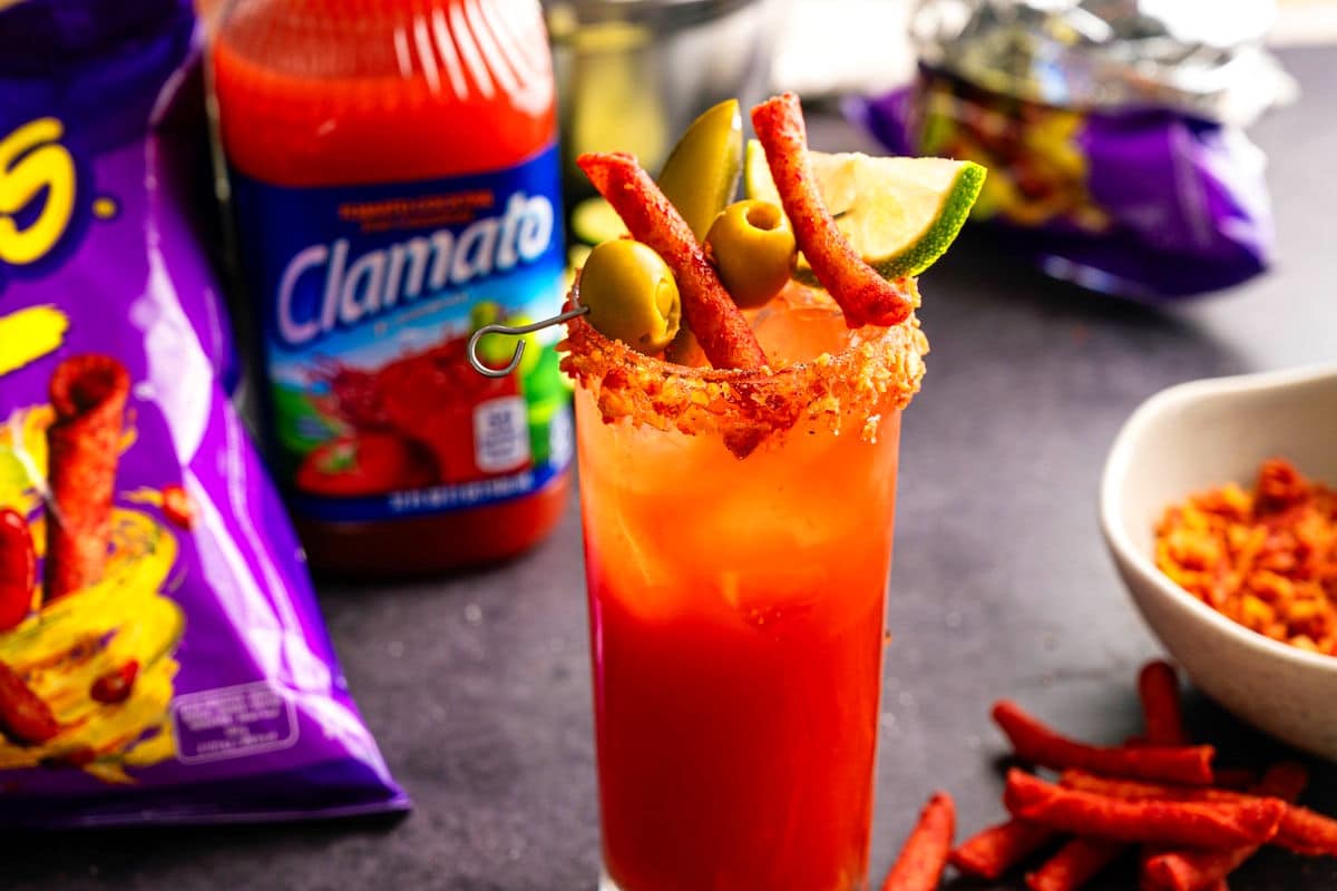 Takis Caesar in a tall glass with Clamato juice and takis chip bag in the background.
