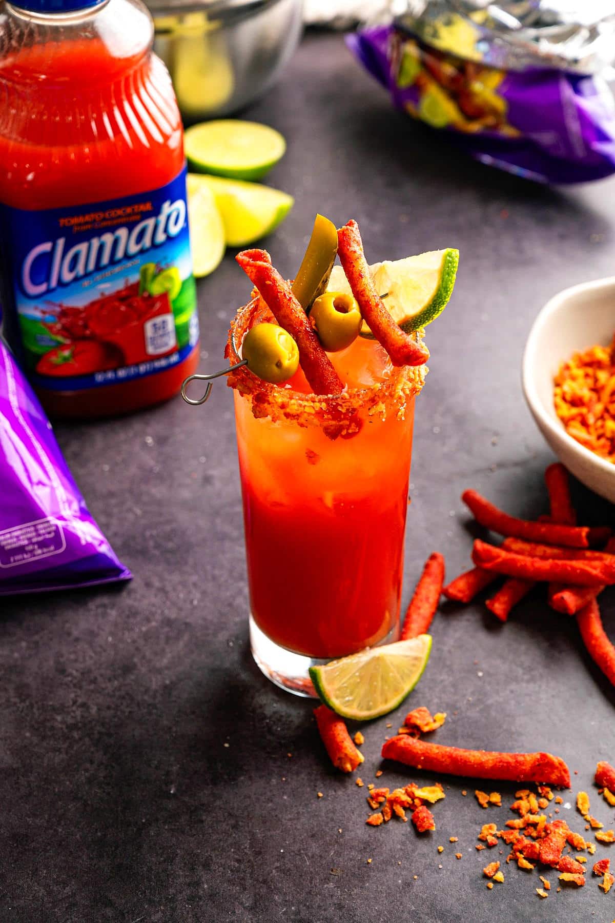 Takis Caesar cocktail in a tall glass with lime and takis chips on the side.