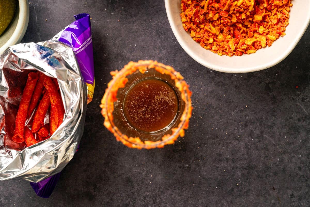 Collins glass with takis rimmer, filled with Caesar cocktail ingredients.