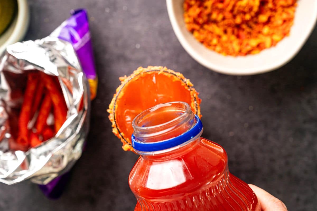 Clamato juice pouring into takis rimmed glass.