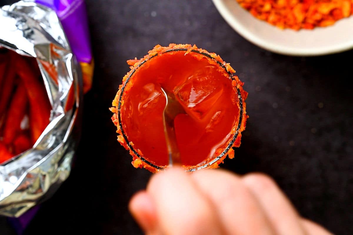 Hand stirring a Caesar cocktail with a long spoon.