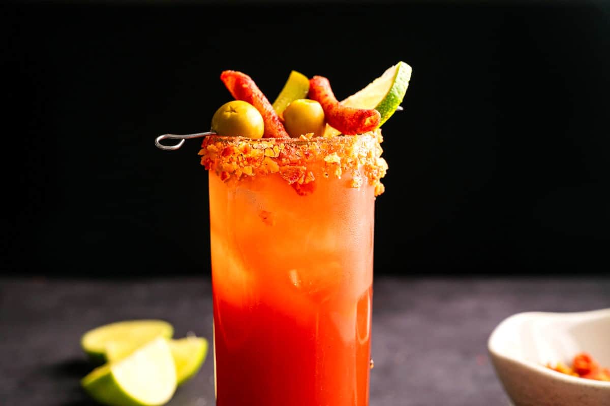 Takis Caesar cocktail in a tall glass with Takis olive skewer garnish.