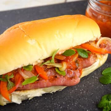 Italian sausage sandwich with peppers and onions on black cutting board.
