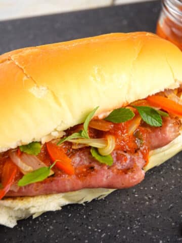 Italian sausage sandwich with peppers and onions on black cutting board.