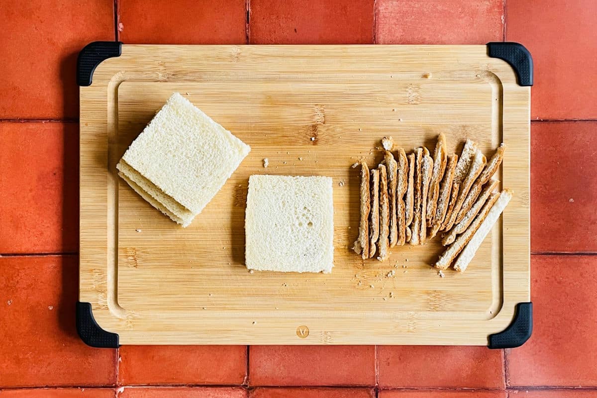 Slices of bread on cutting board with the edges cut off.