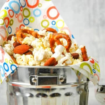 Popcorn snack mix in metal bucket with colorful napkin.